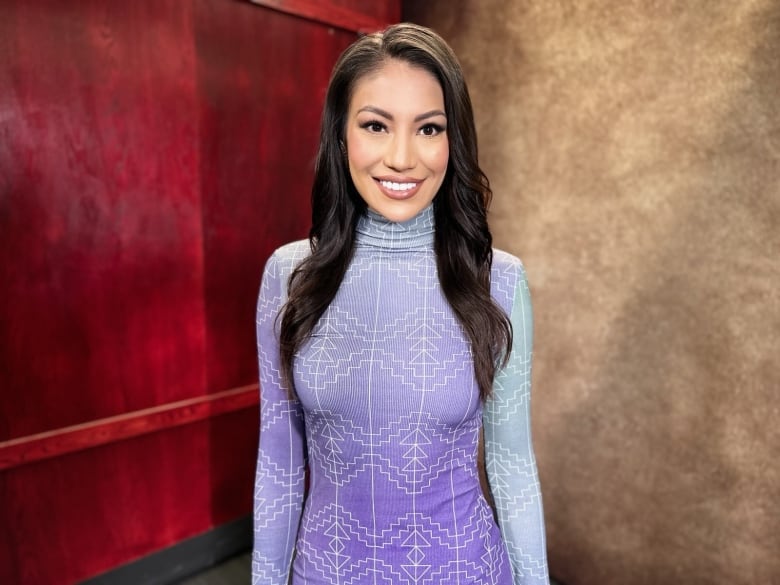 A young woman with long hair poses in a light colored dress and a big smile.