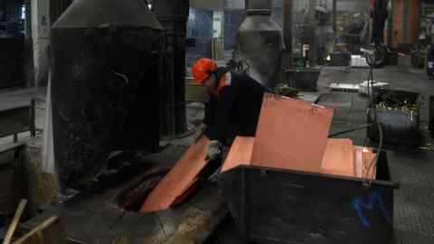 A worker loads copper sheets into a furnace