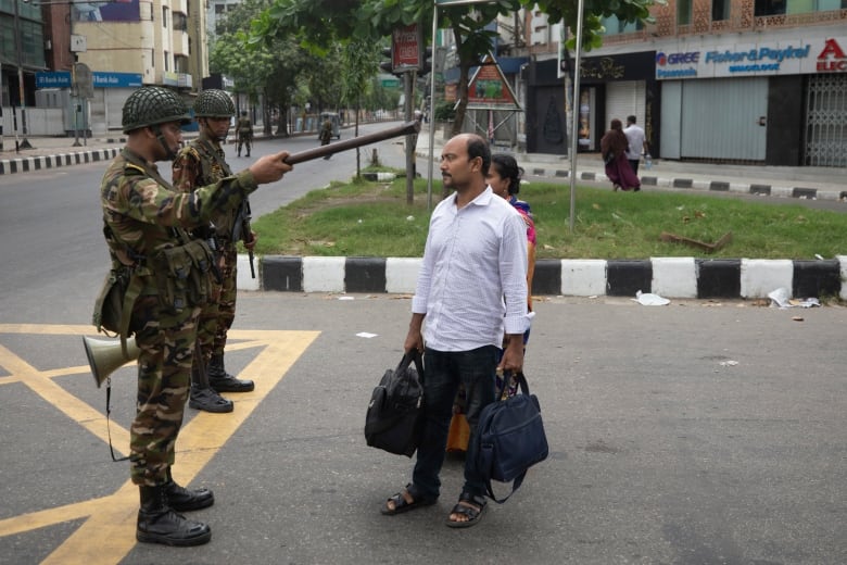 A soldier points a stick at a couple.