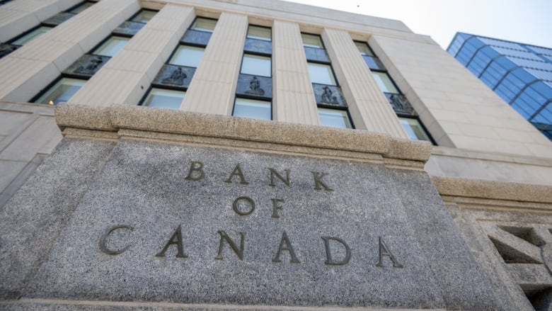 A photo of a white stone building, taken from a very low angle. The sign reads 'Bank of Canada.'