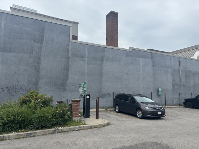 A van is parked next to a large, blank, grey cement wall in a parking lot on an overcast day