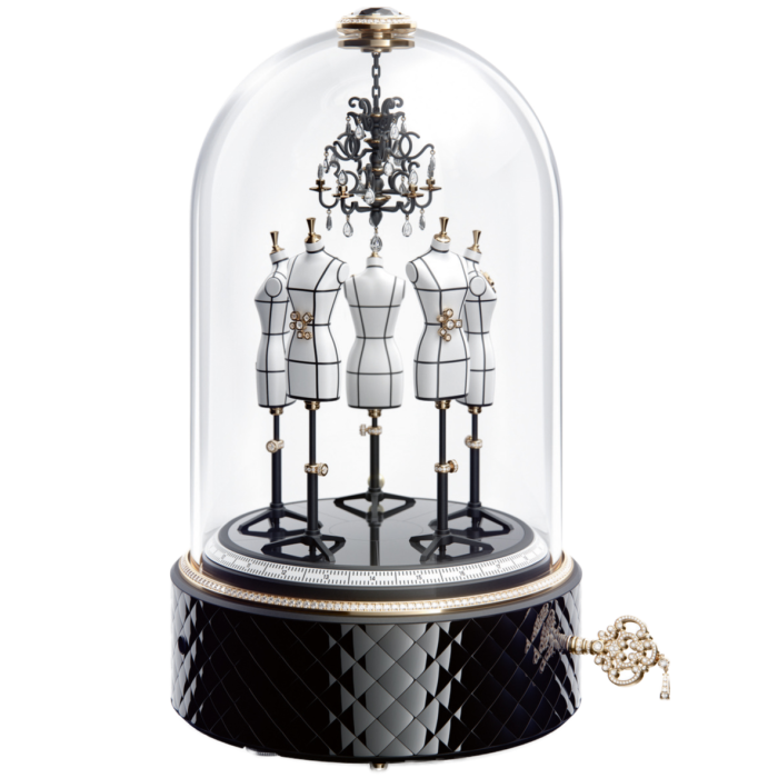 Four miniature dress forms on black metal stands. These are encased in a dome-like glass with a black round base and a turning key at the side. A small miniature hangs from the inside the enclosure, directly above the four dress forms