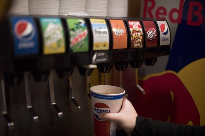 A person holds a pepsi cup under a soft drink dispenser
