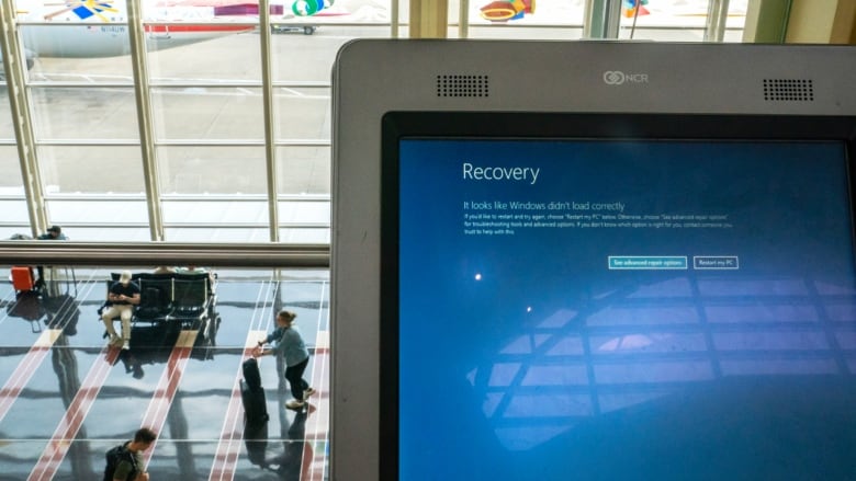 Air travellers are seen in the background of a computer showing the blue screen of death. 