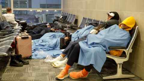 People sleep on bench seats at an airport terminal