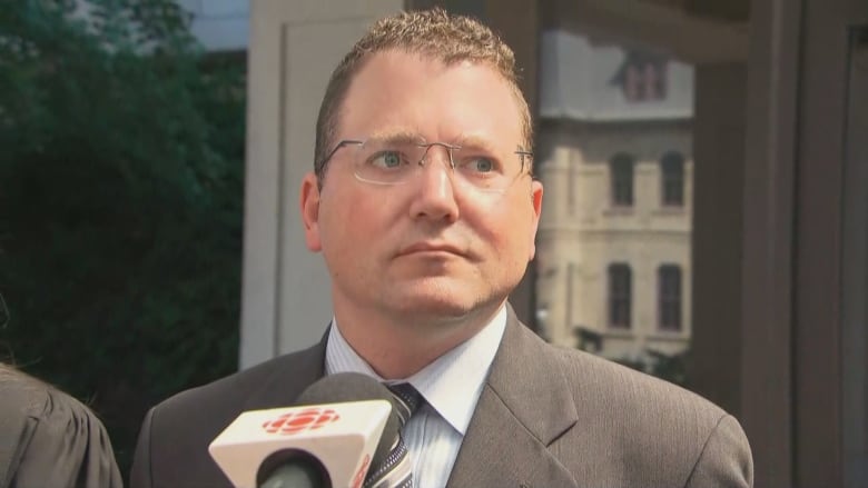 A man in glasses and a suit outside a courthouse on a summer day.