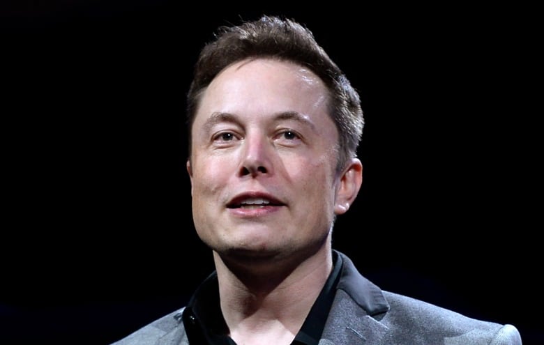 A man in a grey suit gestures while speaking. 