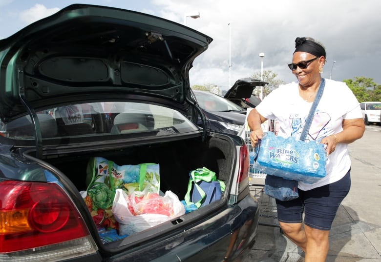 A woman smiles as she loads her car trunk. The plastic wrap on her bottles says "Blue Waters."