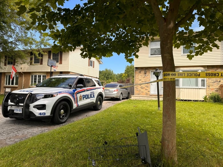 A London police vehicle parked outside a home with yellow police caution tape around the yard. 