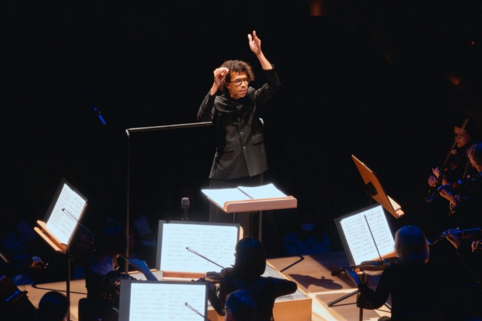 A man in a black jacket raises his hands as he conducts