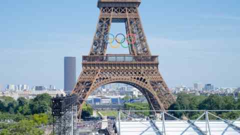 Stands being erected in a square with a  statue of a woman on a winged horse and also at the base of the Eiffel Tower, which bears the symbol of the Olympic rings