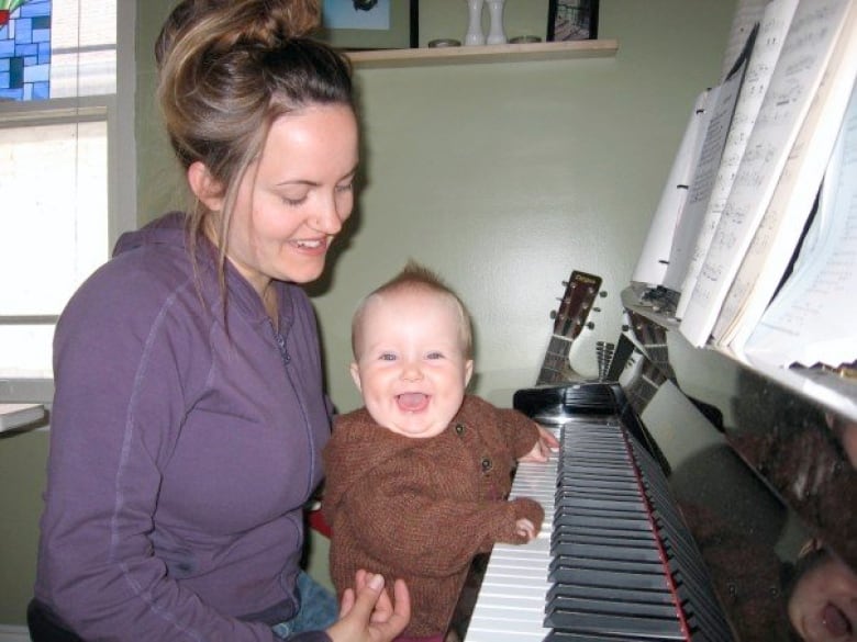 A baby's hands rest on piano keys while sitting on a woman's lap. 