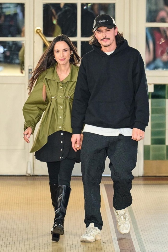 A woman wearing a green top and black skirt and a man wearing a black hoodie takes a bow