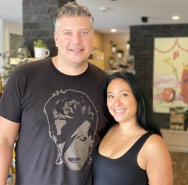 A man in a black tee-shirt stands with his arm around the waist of a woman in a black dress.