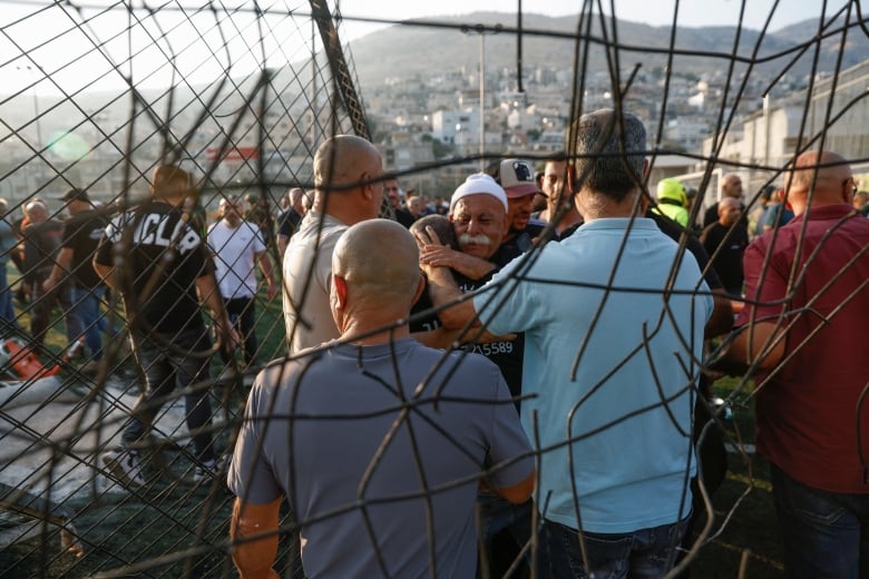 A group of people react and embrace at on a field.