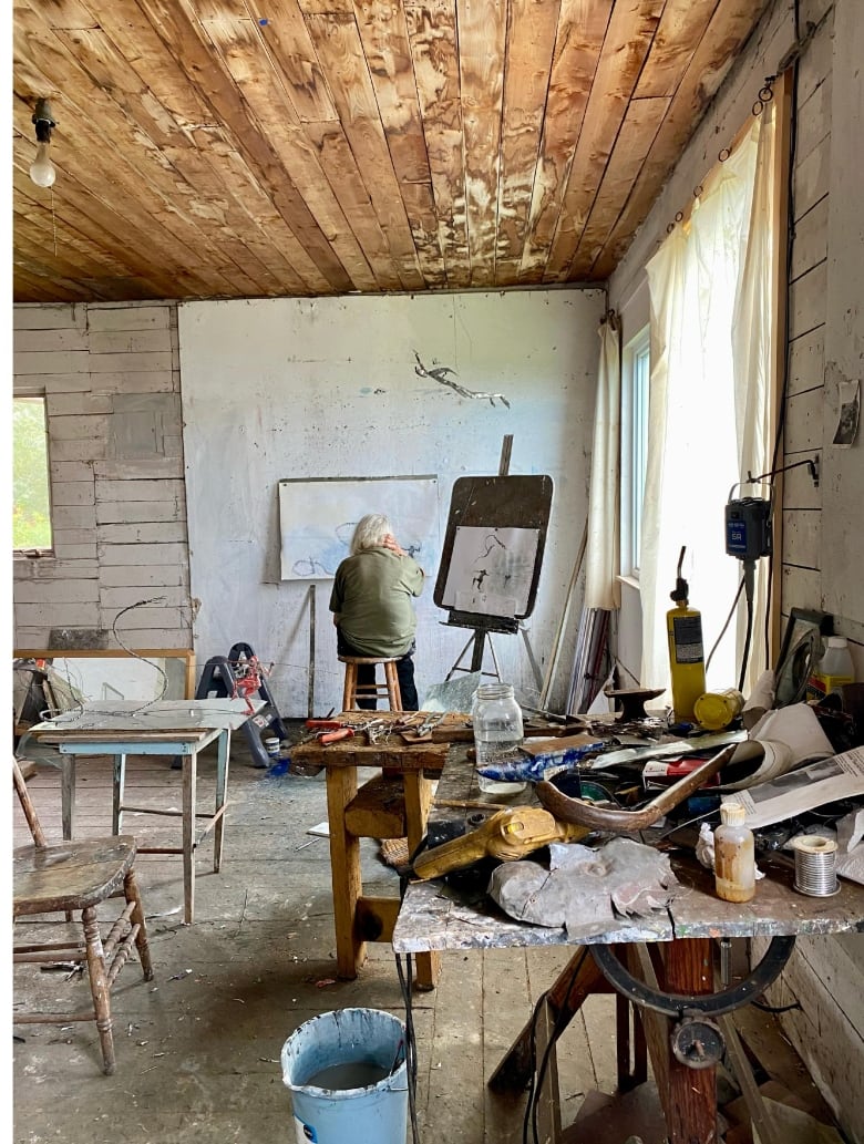 A woman sits in front of an easel in an art studio.