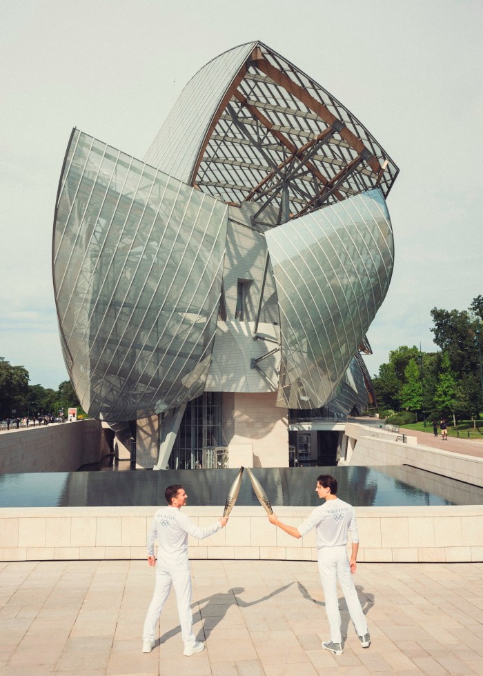 Two athletes pass on a flame with Olympic torches in front of an art gallery