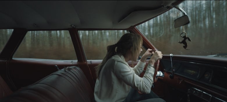 A woman sits in a car. She appears to be screaming. 