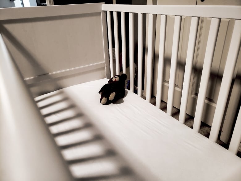 White crib with a old teddy bear.