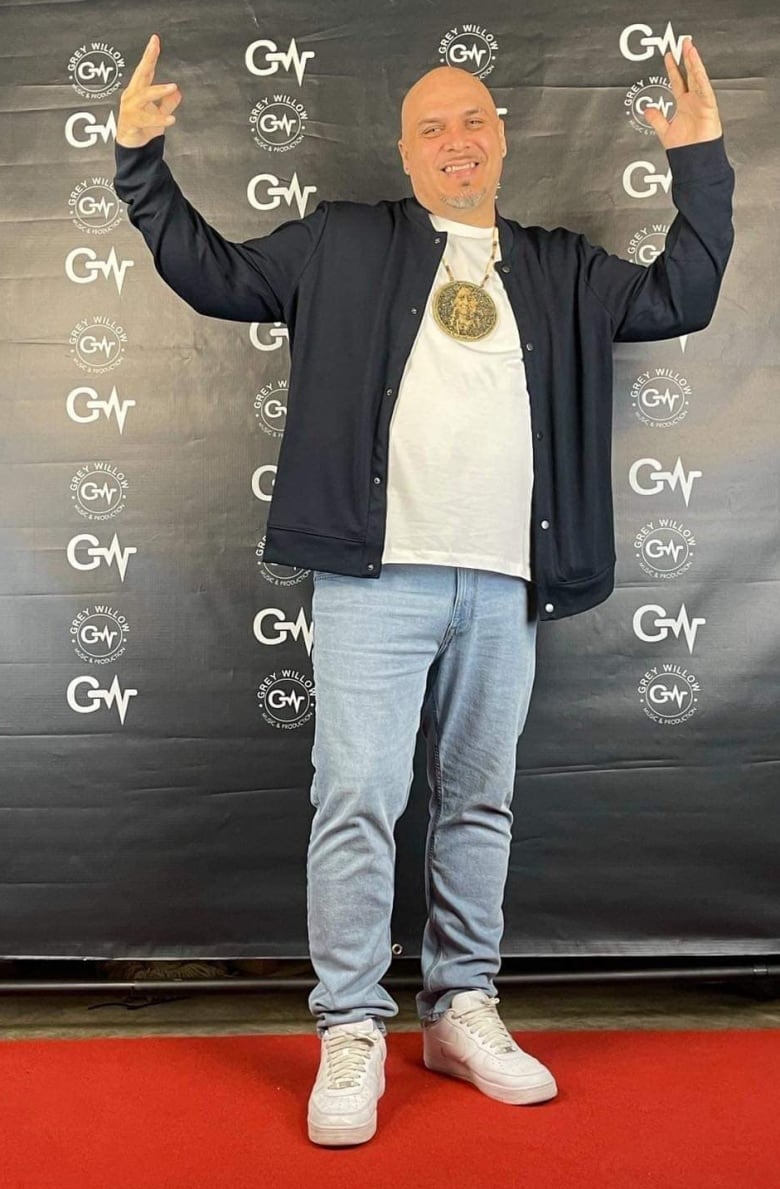 A man wearing a beaded medallion poses on a red carpet.