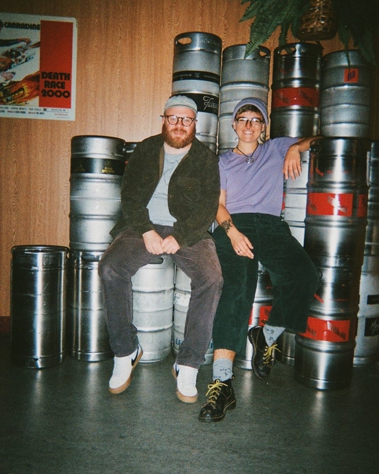 Two people sitting on a stack of kegs.