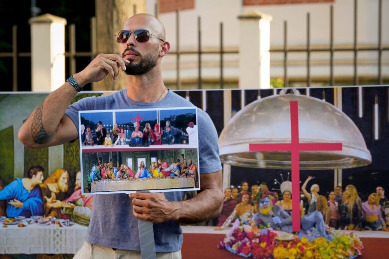 A man holding a  sign stands in front of a tableau