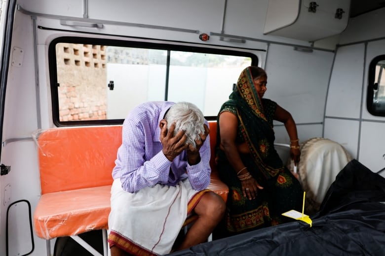 A man puts his head in his hands and sits beside a woman in an ambulance.