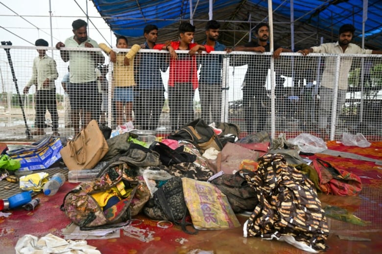 A row of men stand behind a fence and look at a pile of belongings.