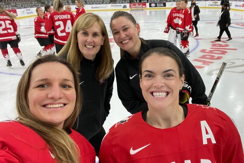 Four women in Team Canada gear pose on the ice.