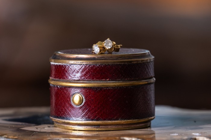 a pair of earrings with diamonds placed on top of a round case that appears to be made of leather