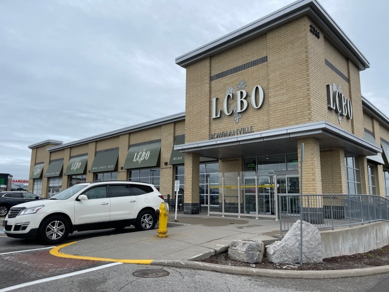 A white SUV is parked outside a brick building with a sign that reads Bowmanville LCBO.