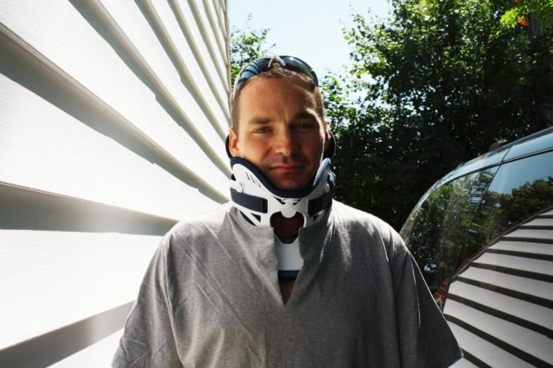 Man wearing a collar brace stands outside by a vehicle.