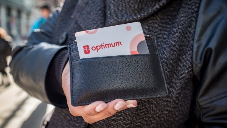 A person holds a black wallet with a white and red card sticking out of it.