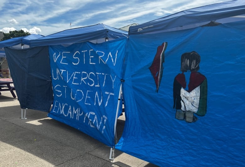 Blue tarps with the words "Western University Student Encampment" and a painting of a person wearing a Palestinian flag as a cape.