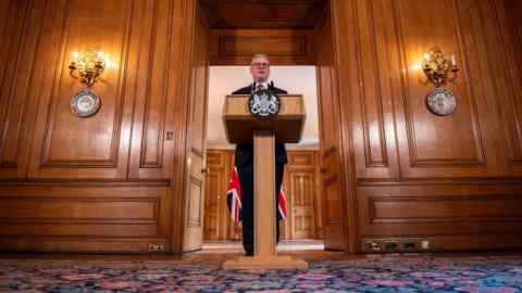 Keir Starmer speaks from behind a podium in a wood-panelled room in Downing Street