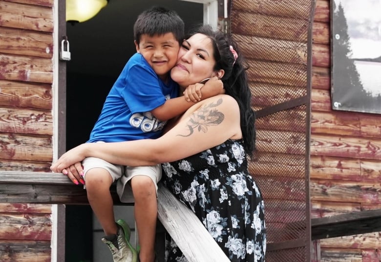 A women and a son hug in front of a brown building. 