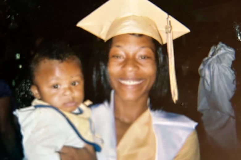 A person wearing a graduation cap and gown smiles while holding a baby.