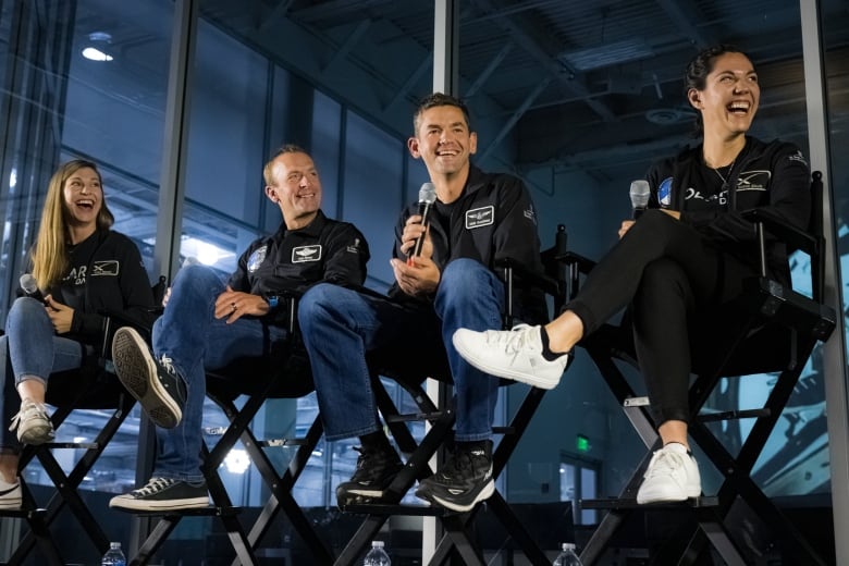 Four people are seen on a stage smiling.