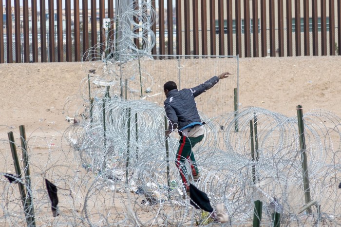 A man climbs along a barbed wire fence