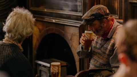 A man wearing a flatcap sipping beer by the fireside in Sandy’s Bell pub, Edinburgh