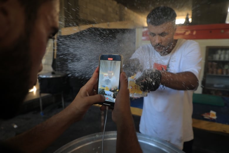 A man records another man opening a bag of white powder to cook with in a pot