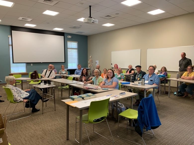 Group of adults are in a classroom and smiling at a camera. 