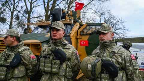 Turkish soldiers walk beside an armoured vehicle