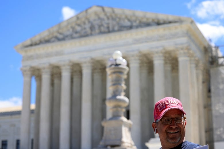 Man with Trump cap smiles in front of court