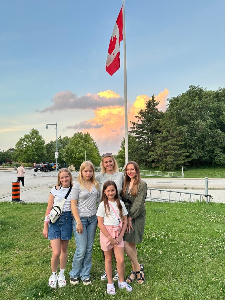 Three girls and two women pose for a picture with a Canadian flag behind them