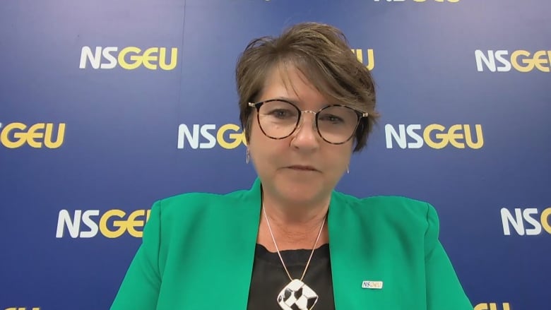 Short haired woman sits in front of a background with multiple NSGEU logos. 