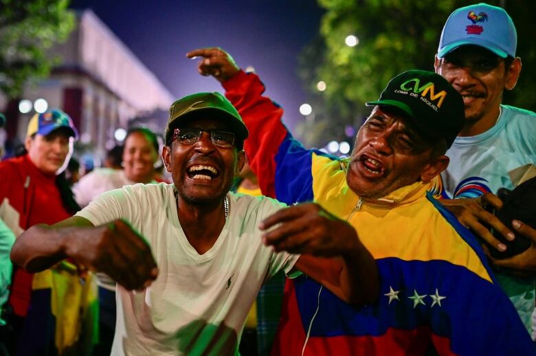 A group of men in green caps laugh and raise their arms in the air.