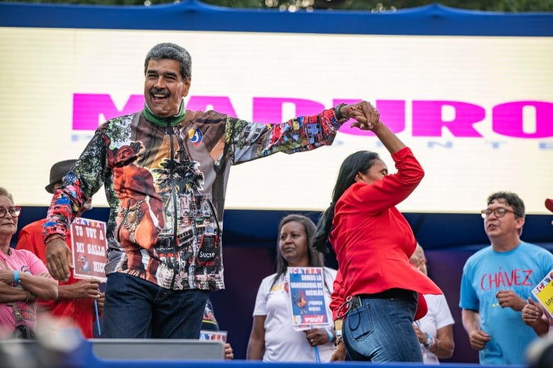 A mustachioed man in a loud, multicolored shirt holds his arm aloft with a woman who does a dance turn.