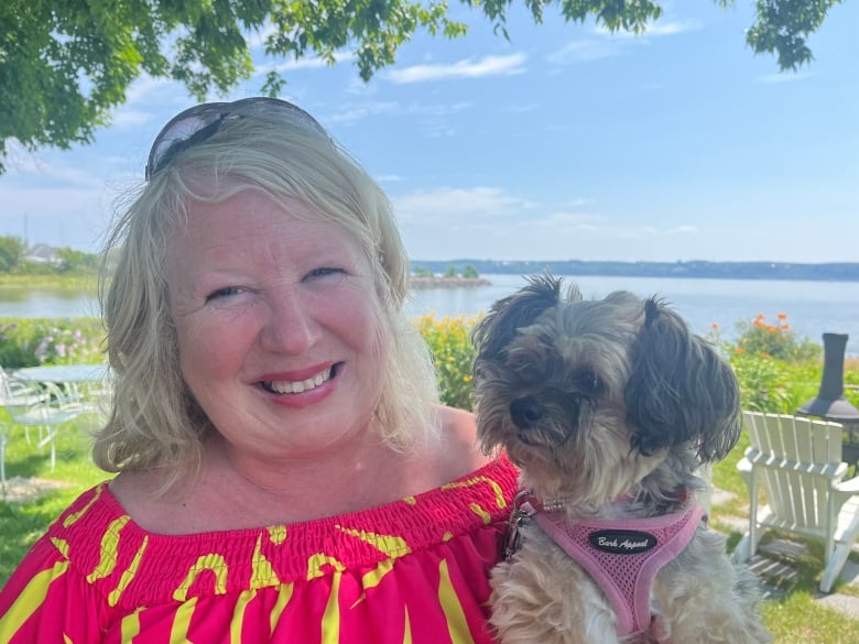 A woman with sunglasses on her head holding her small dog. 