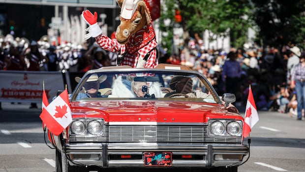 A red convertible with Canadian flags on the headlights drives along with someone in a horse costume in the back